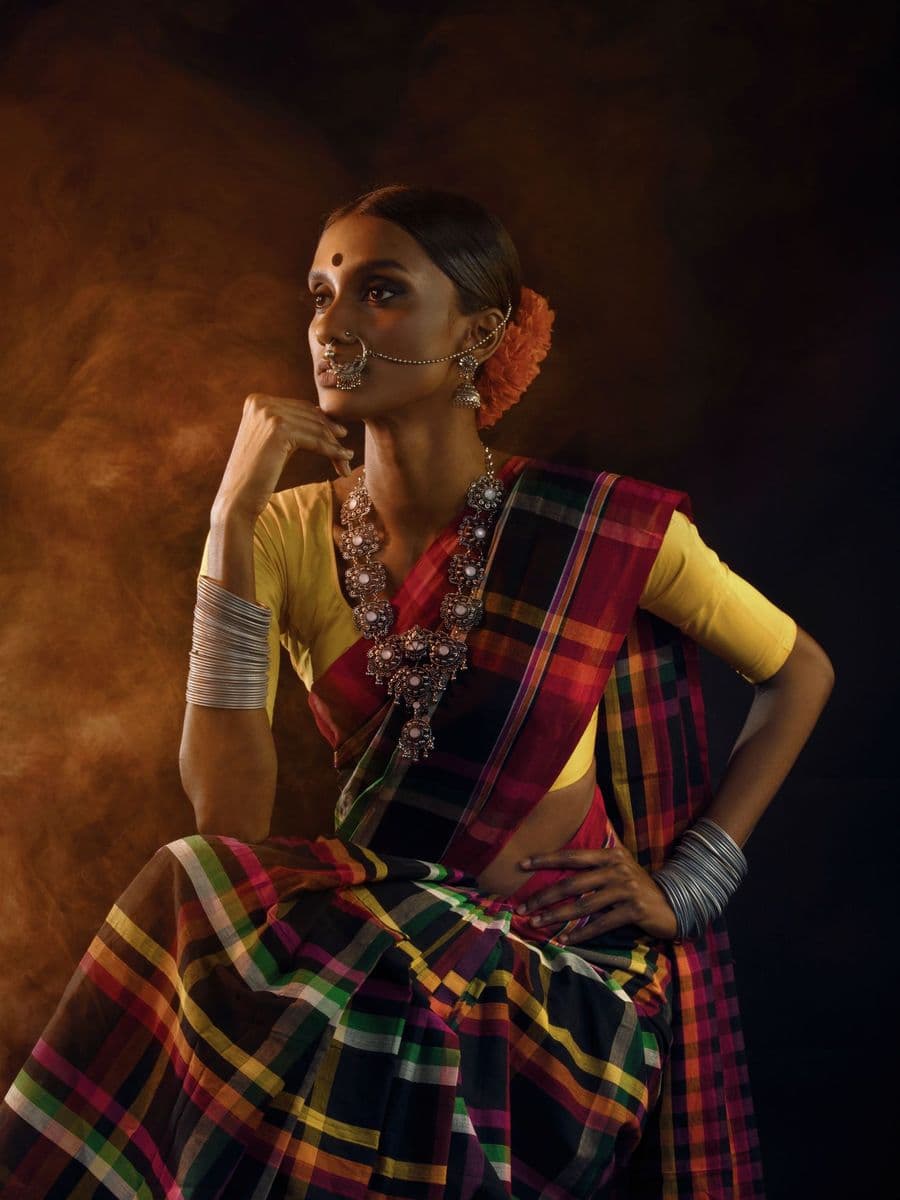 Indian woman in a checked silk saree and silver jewellery posing against a dark amber studio backdrop
