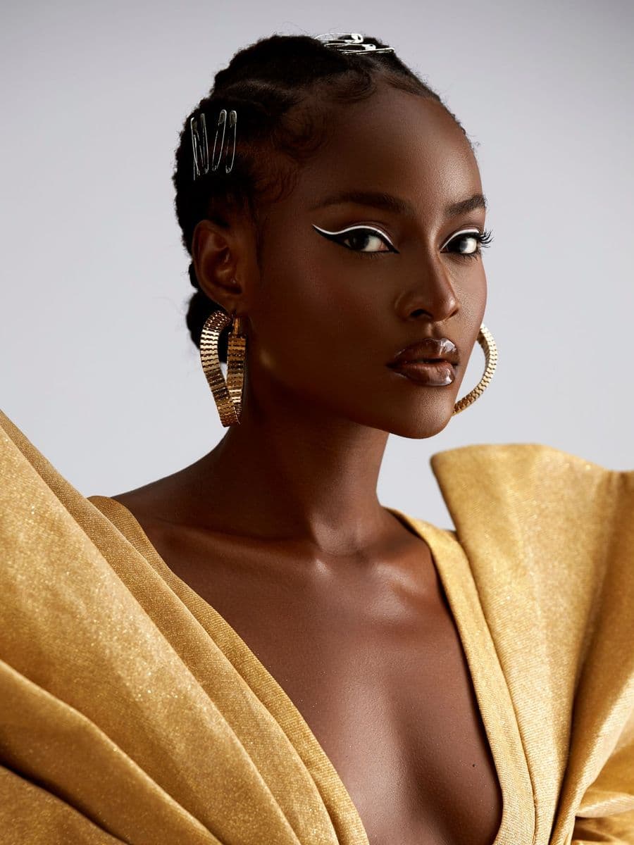 Black woman with braided hair, gold hoop earrings and a gold draped garment in a studio portrait
