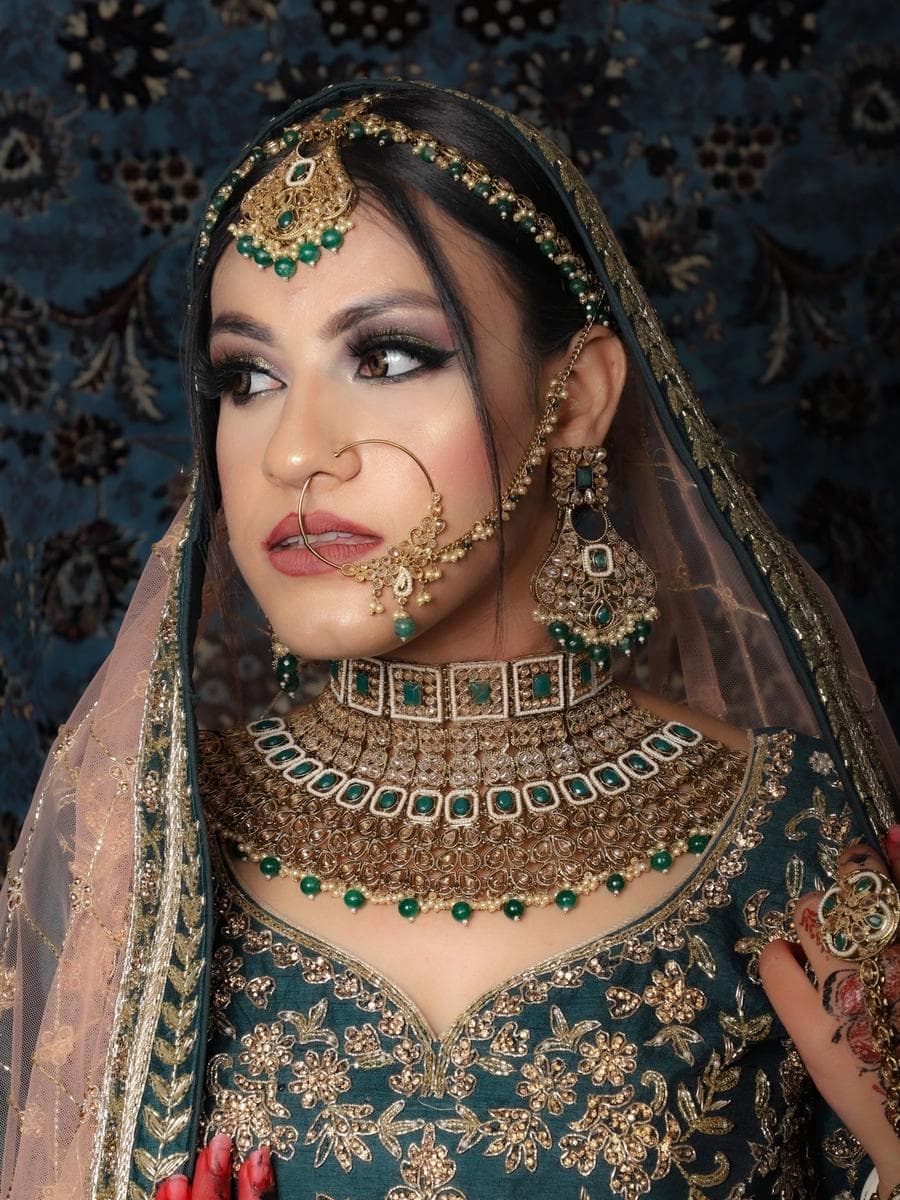 Indian bride in a green and gold lehenga with a nose ring and heavy emerald necklace