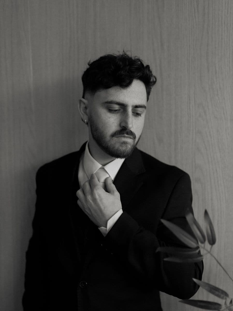 Black and white portrait of a bearded man in a dark suit adjusting his collar