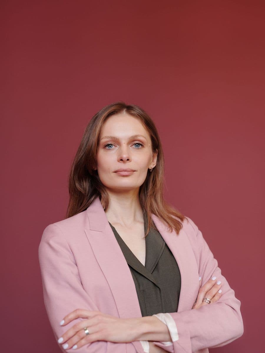 Woman in a pink blazer with arms crossed against a deep red wall