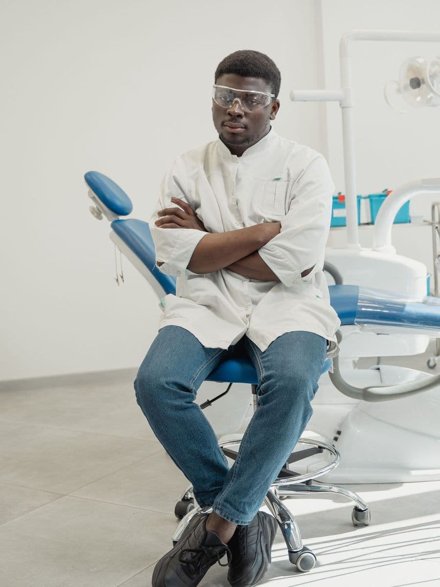 Dentist in a white jacket sitting with arms crossed in front of a dental chair