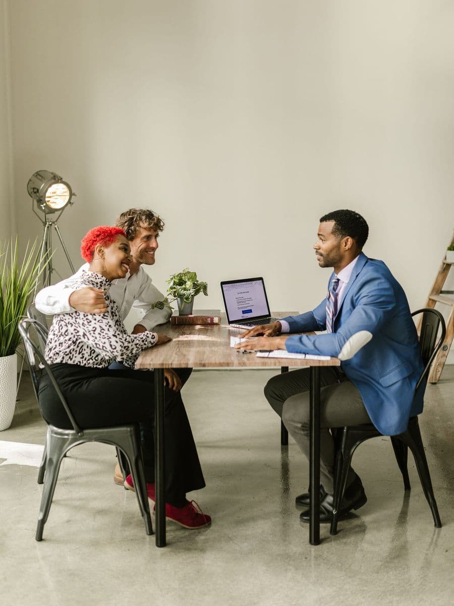 Adviser in a blue suit talking with a couple across a table with a laptop