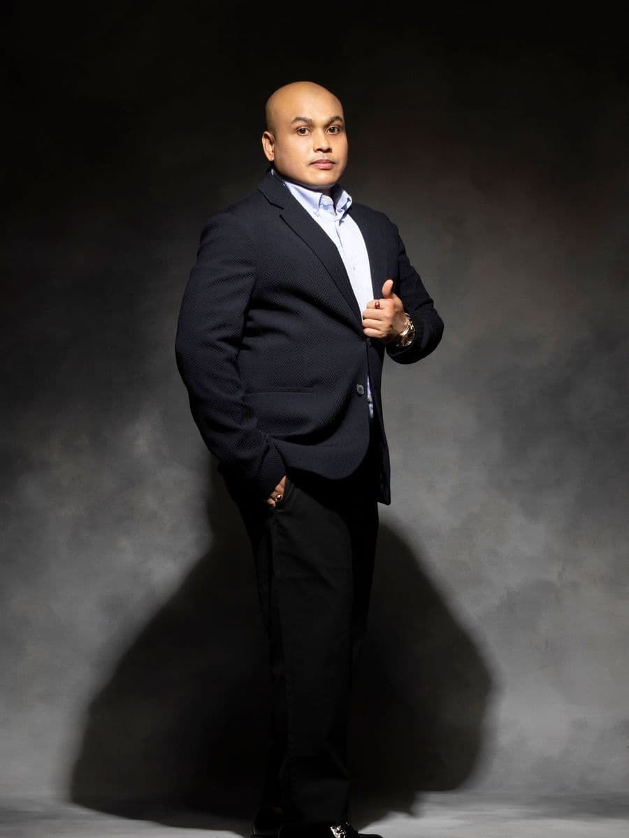 South Asian man in a black suit standing confidently in a studio
