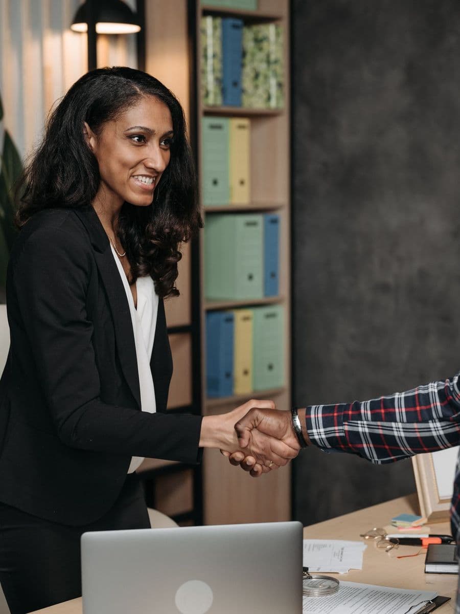 Smiling woman lawyer in a black suit shaking a client's hand in an office lined with files