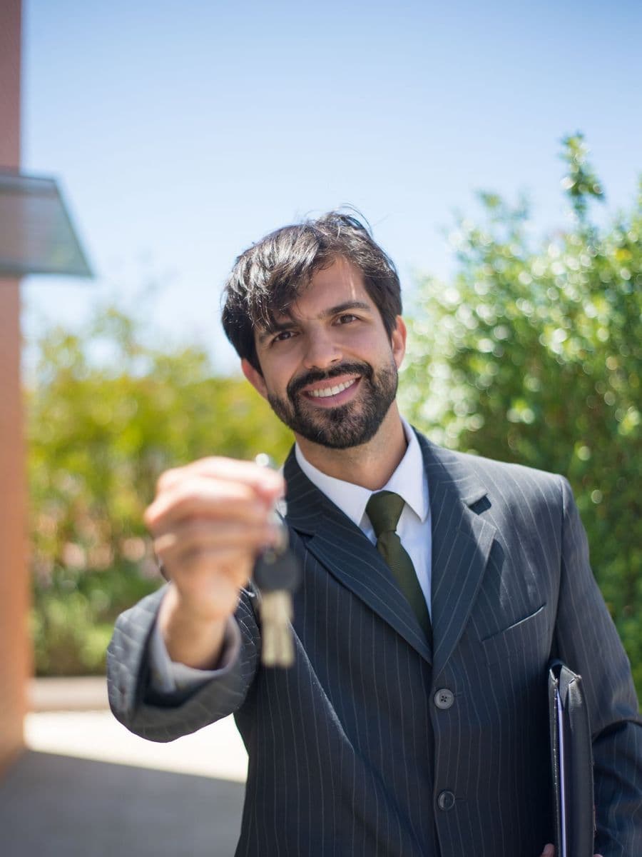 Smiling estate agent in a pinstripe suit holding out a set of house keys