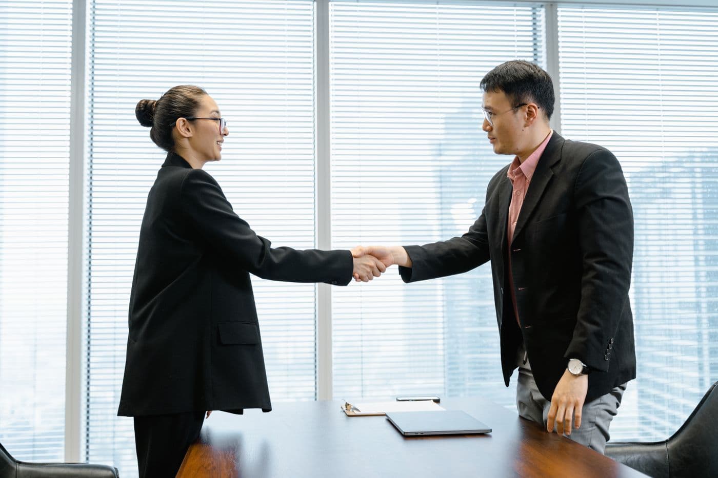 Woman and man in business suits shaking hands in a bright glass-walled office