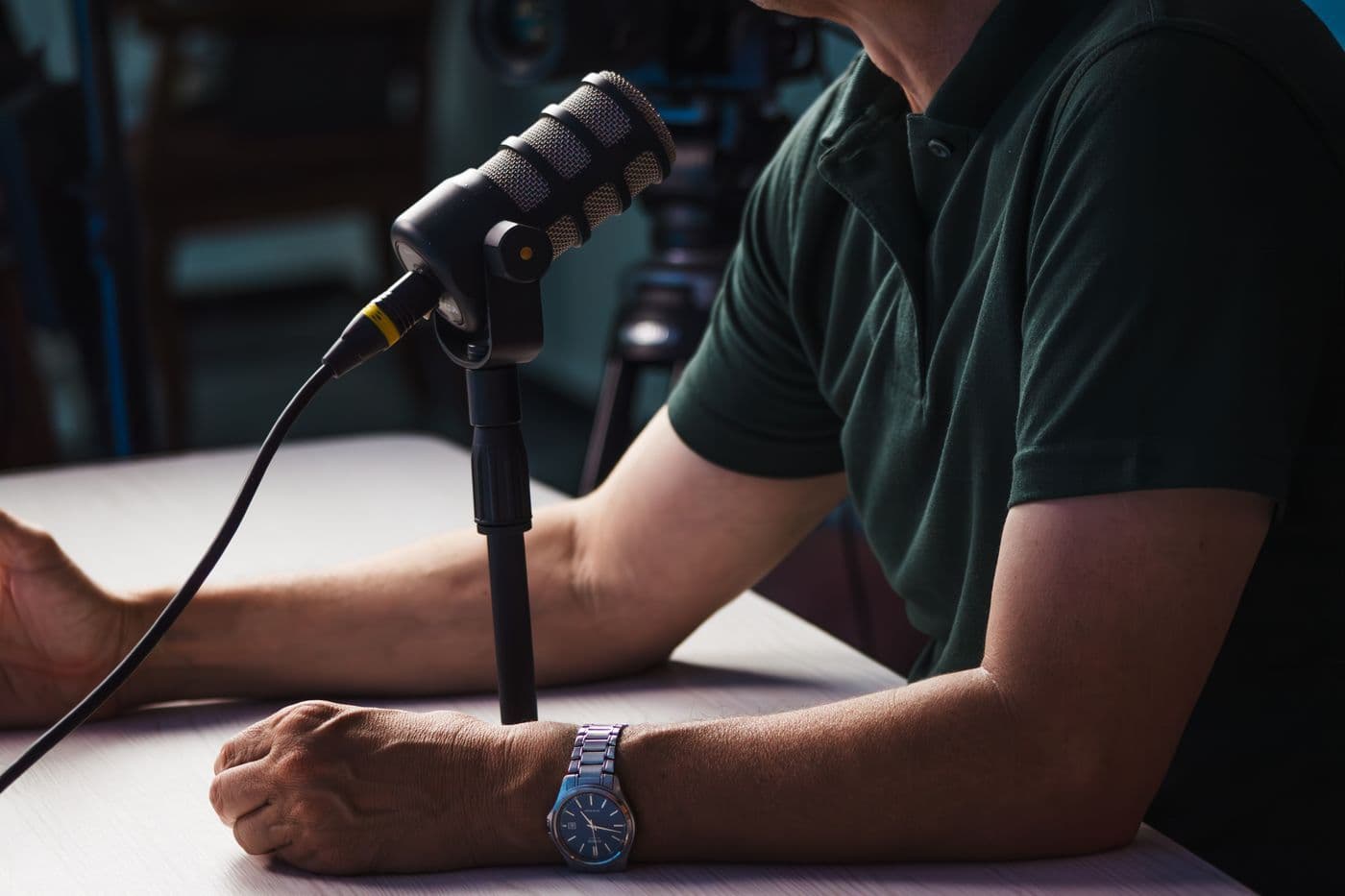 Person seated at a table speaking into a podcast microphone on a stand