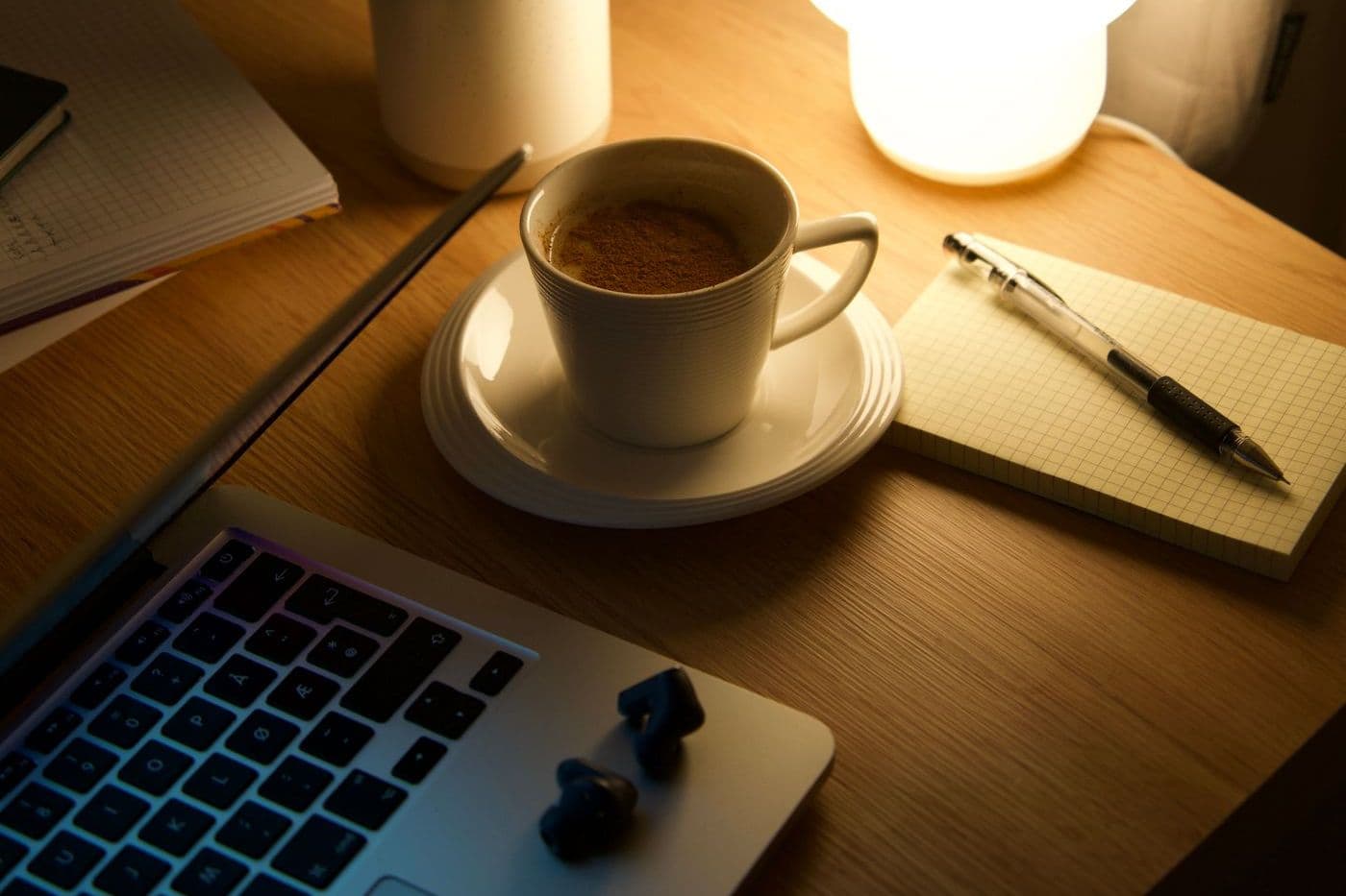 Warm-lit desk with a glowing lamp, a cup of coffee, a notebook and a laptop