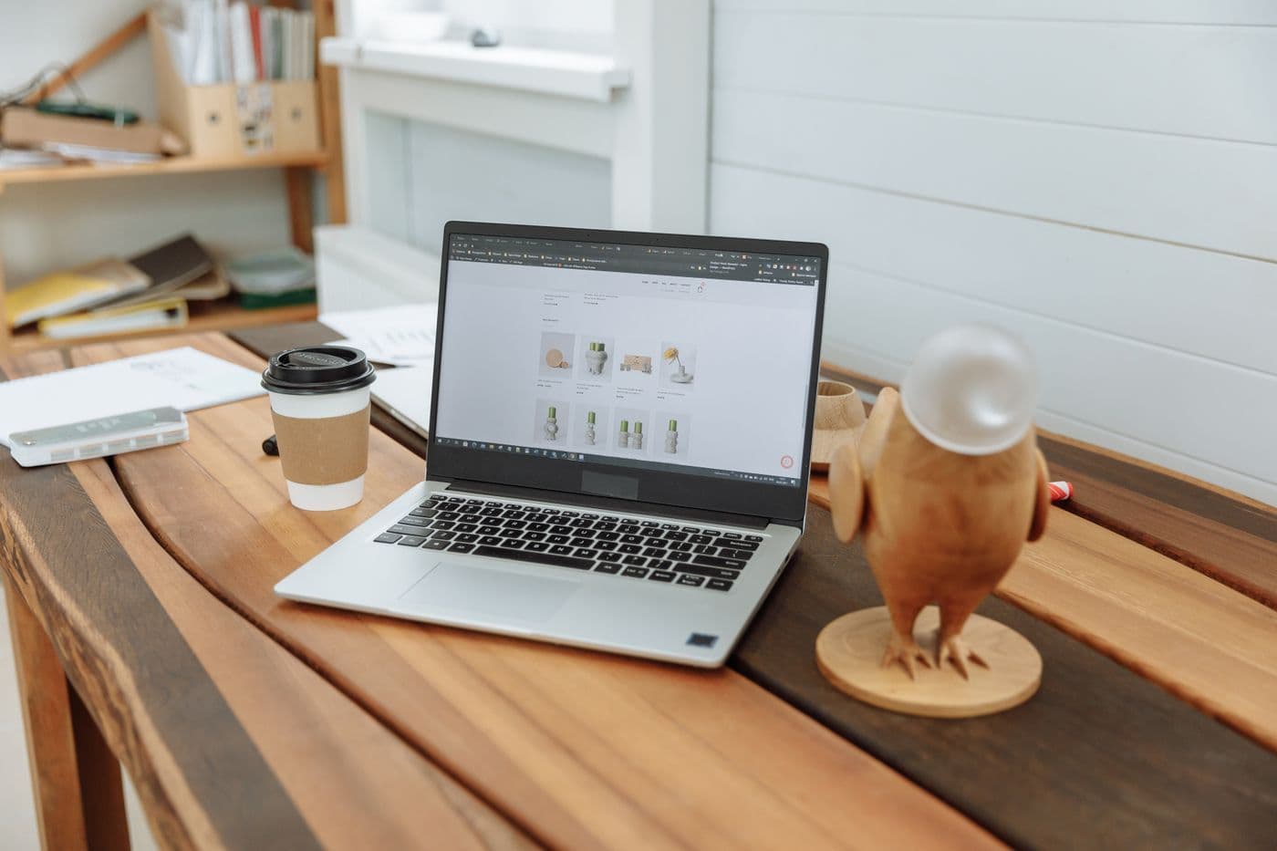 Laptop showing a product website on a wooden desk beside a takeaway coffee cup
